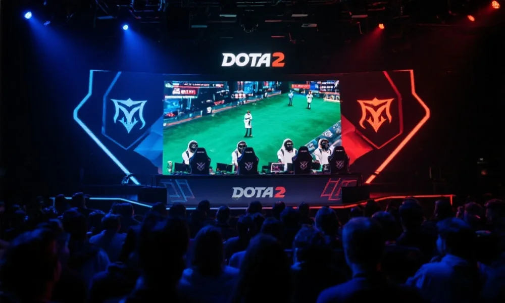 现代电竞舞台上,观众聚焦于大屏幕正在直播DOTA2比赛,选手们专注操作